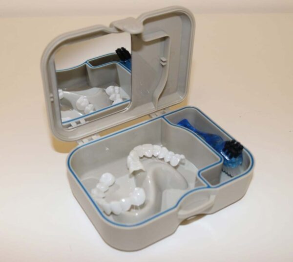 An open storage box containing a set of dental veneers, along with a cleaning brush and mirror