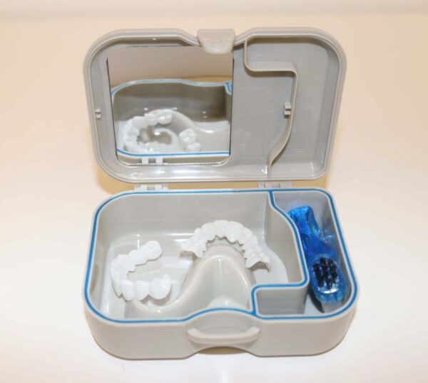 An open storage box containing a set of dental veneers, along with a cleaning brush and mirror